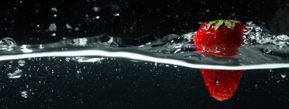 Side view banner of water splashing on dark background with strawberry