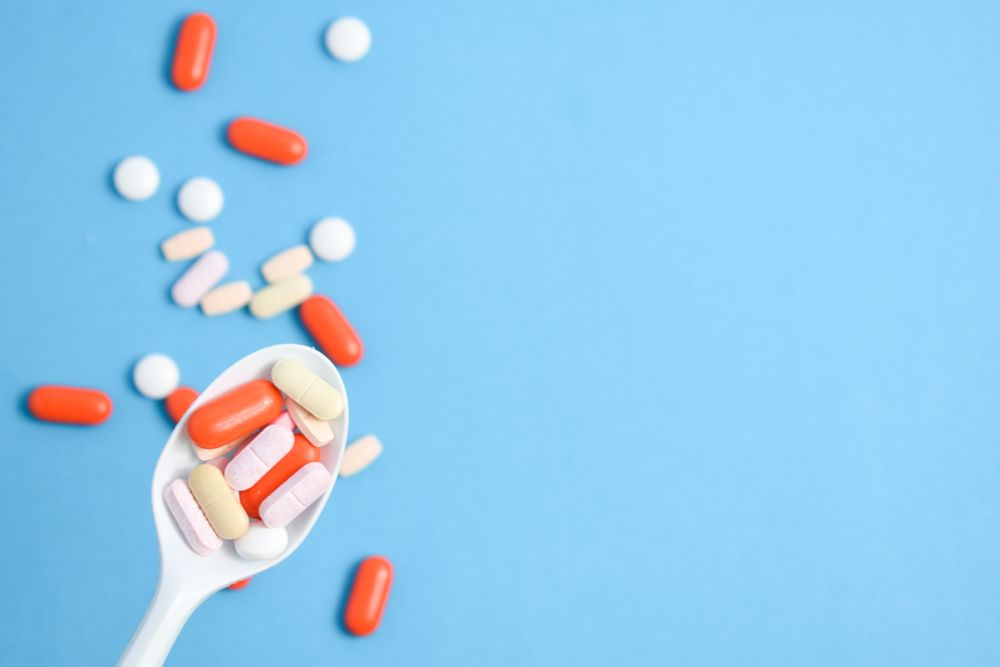 Plastic spoon with various colorful pills over blue table