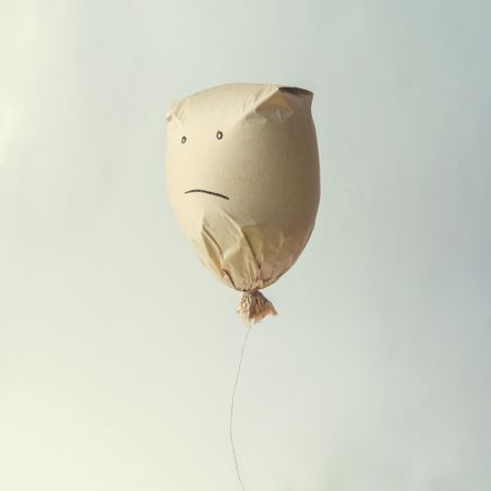 Paper bag balloon with sad face on light background