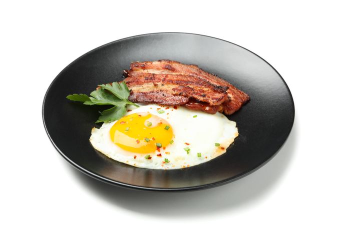 Plate with fried egg, bacon and garnish