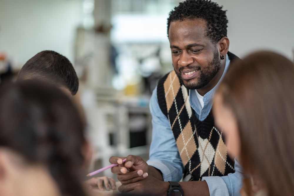 Male teacher with students in classroom holding pencil