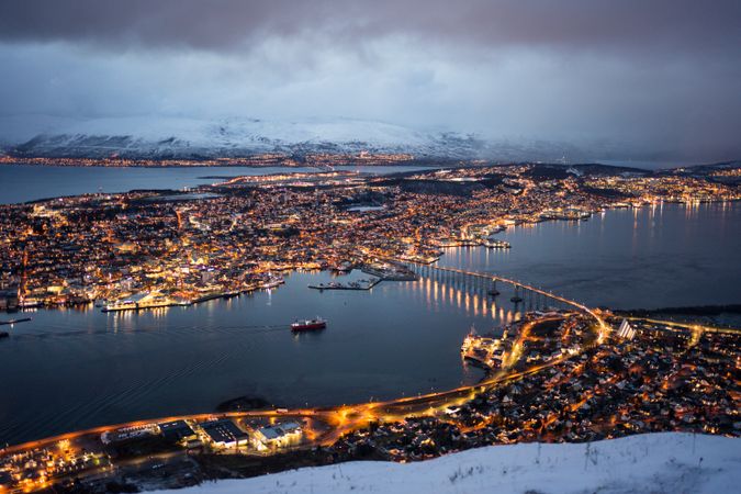 Majestic view of night city against snowy mountains in overcast weather