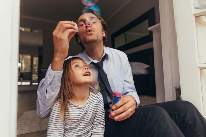 Man sitting with his daughter and blowing soap bubbles