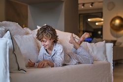 Cheerful boy creating sketch in paper notepad at home