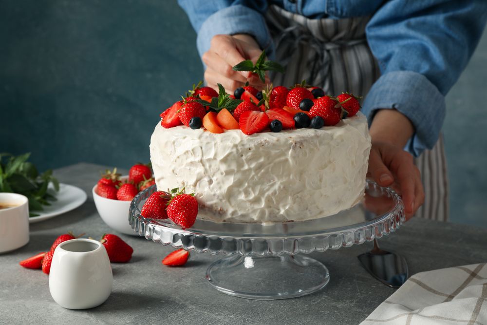 Woman puts mint on berry cream cake. Delicious dessert