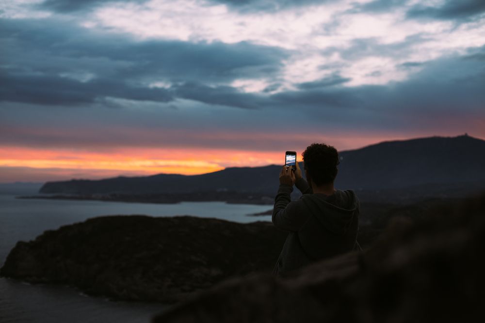 Male with smartphone overlooking the ocean at dusk