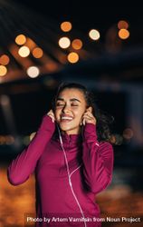 Woman in dark red sport searing smiling while listening to headphones outside 5nq3M0