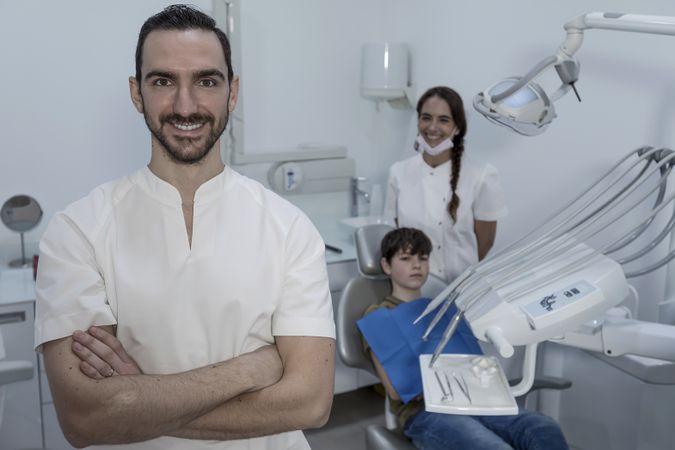 Portrait of a dentist with young teenage patient in background