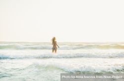 Rear shot of long haired woman in bikini in waves at the beach 0VEmkb