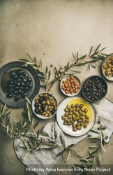 Variety of olives in bowls with branches and linen on concrete background, copy space 0K31V0