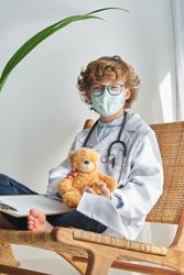 Boy doctor with toy bear on chair on white background