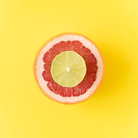 Red grapefruit and lime slice on pastel yellow background