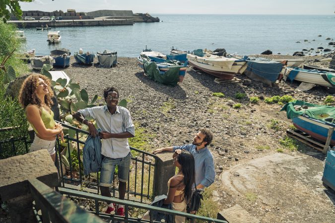Group of diverse friends pausing on stairs to talk and enjoy the sea view in Sicily, Italy.