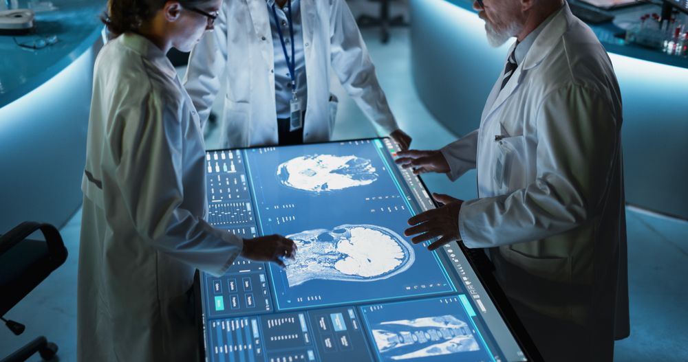 Modern Hospital Medical Research Center: Diverse Colleagues Gathered Around Interactive Touch Screen Table With CT Scans Of Brain On Display.