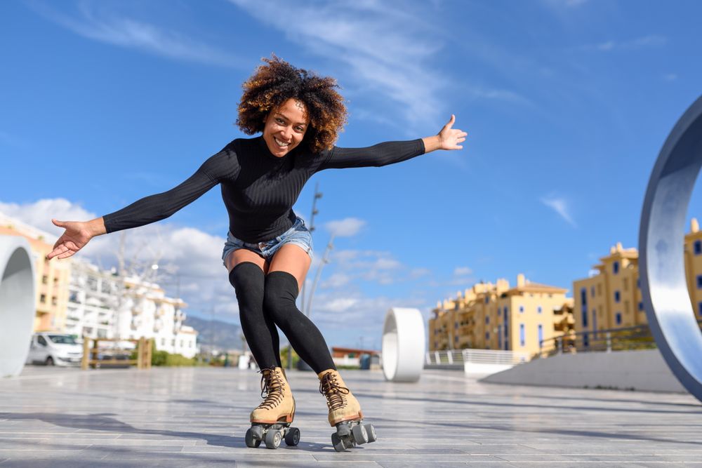 Happy woman with afro and arms spread roller skating outside