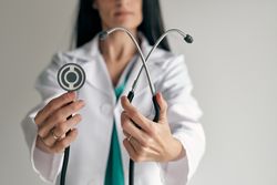 Crop physician showing stethoscope on light background
