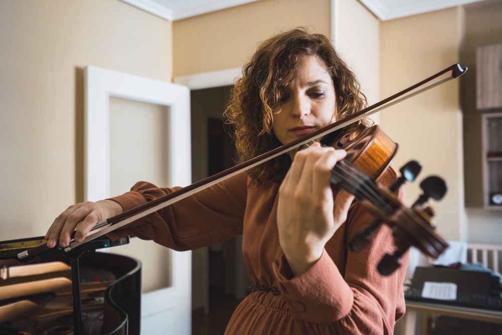 Pregnant woman playing on violin near piano in room