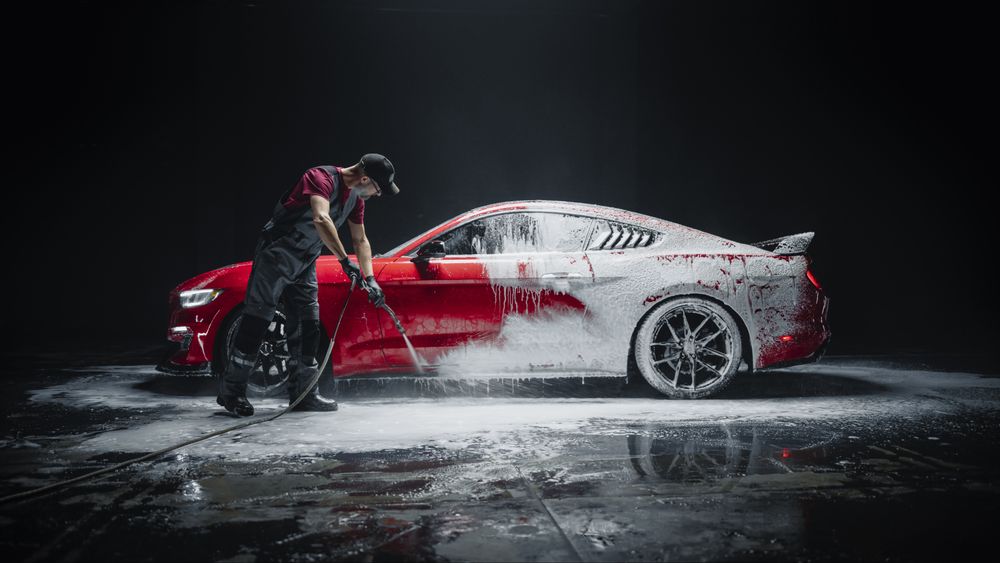 Car Wash Specialist Using Pressure Washer to Rinse a Red Modern Sportscar.