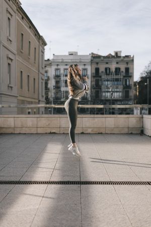 Full length side view of woman jumping with her arms across her chest on a roof top