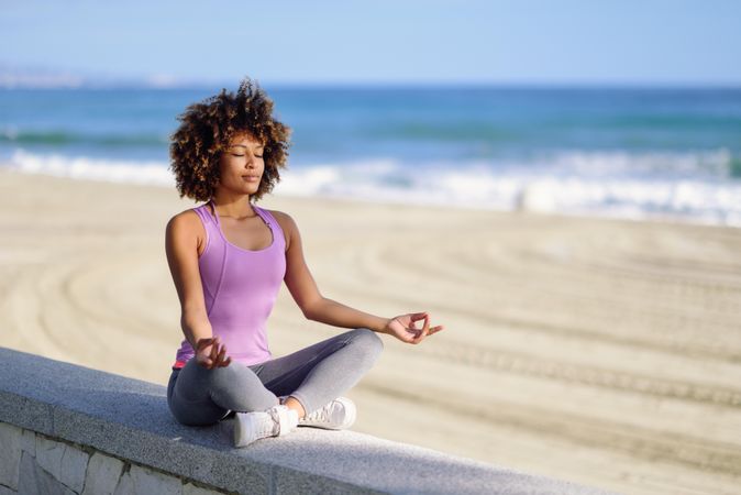 Black woman with afro hairstyle meditating on the beach