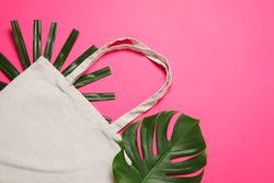 Eco bag and palm leaves on color background, copy space