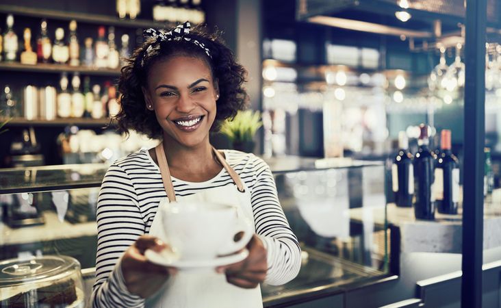 Smiling woman serving a cup of coffee in front of a modern bistro