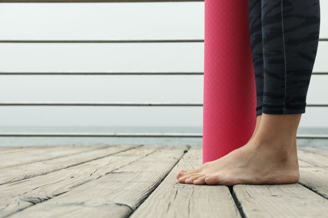 Female legs and yoga mat on wooden floor outdoors, space for text