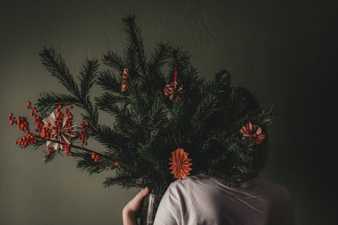 Back view of a person holding pine tree leaves decorated with Christmas ornament against gray background
