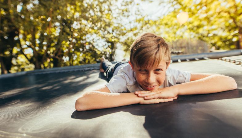 Little boy resting on trampoline after playing outdoors