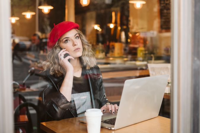 Woman with laptop using smartphone in cafe
