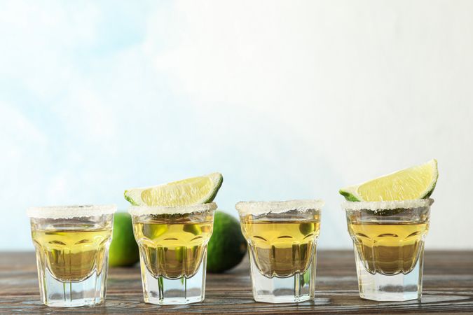 Tequila shots with salt and lime slices on wood table, space for text