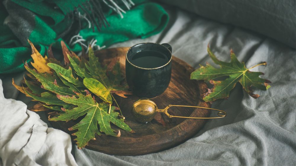 Fall leaves next to tea cup and infuser on wooden tray