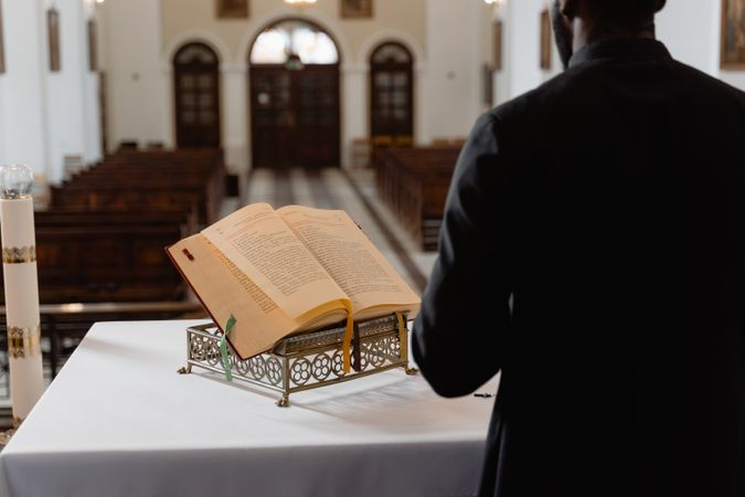 Back view of priest standing beside Bible at the altar