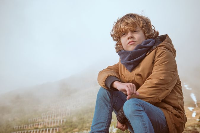 Boy in outerwear sitting against steam clouds