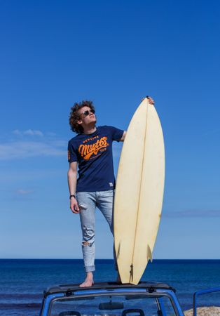 Man with surfboard standing on roof of car