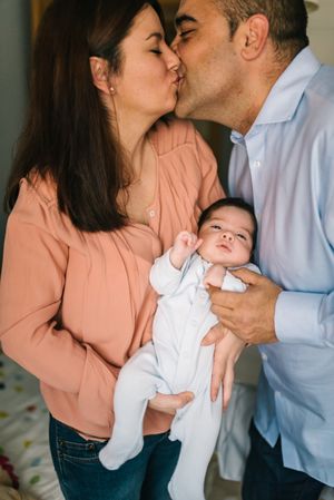 Happy family holding baby and and kissing at home together