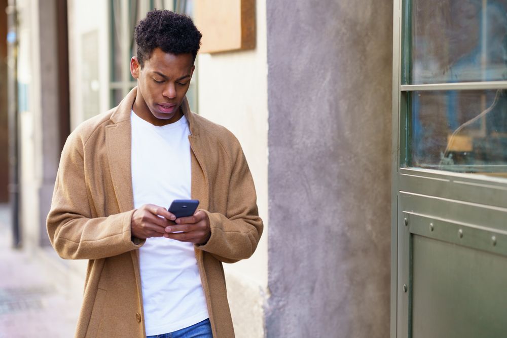 Cuban male typing on his phone while walking