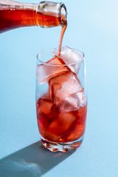 Pouring strawberry syrup over ice in a glass