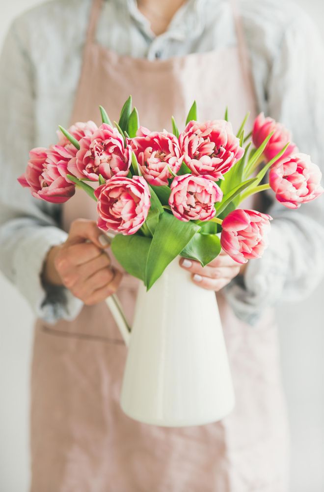 Florist wearing pink apron holding vase with bright spring flowers