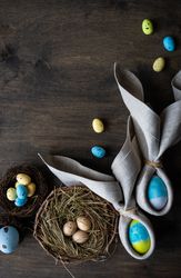 Easter eggs wrapped with rabbit ears with napkin with nest on wooden table