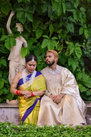 Man and woman in saris sitting on bench beside tree and statue