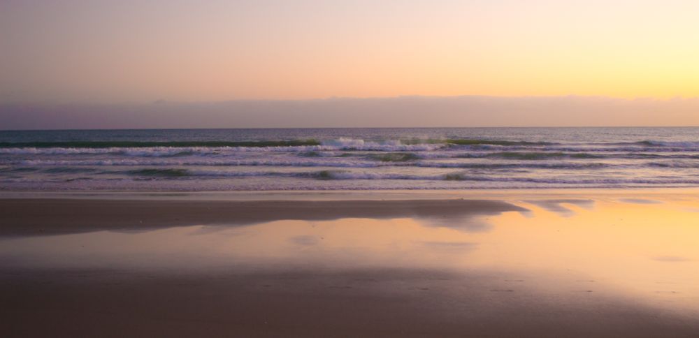 Ocean waves crashing on sand shore under pinkish sky
