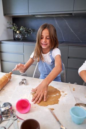 Delighted kid touching raw dough with floury hands and smiling