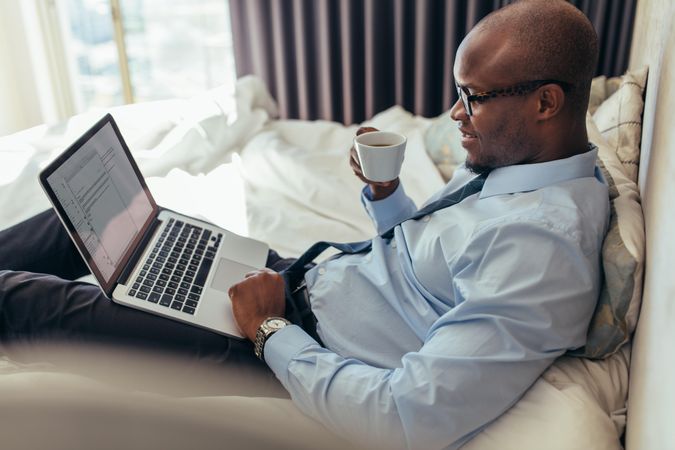 Man in business casual clothes working on laptop while lying in bed