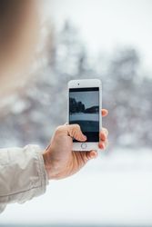Hand taking photo of wintry scene with phone, vertical