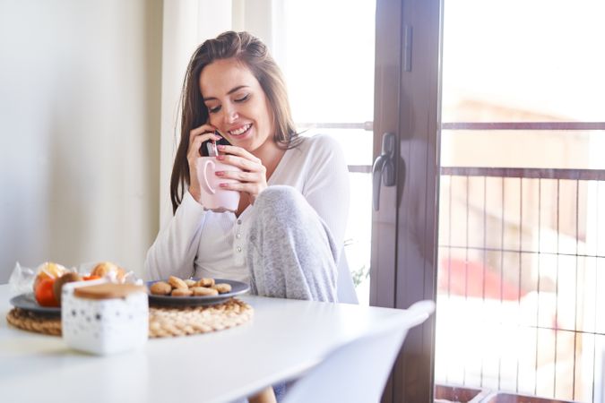 Smiling woman with smartphone eating at table at home