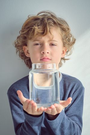 Cute boy holding glass jar with water