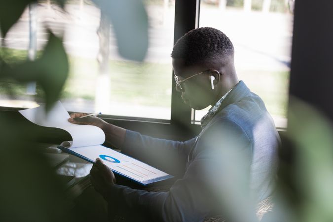Serious Black businessman in earbud with diagram on paper indoors
