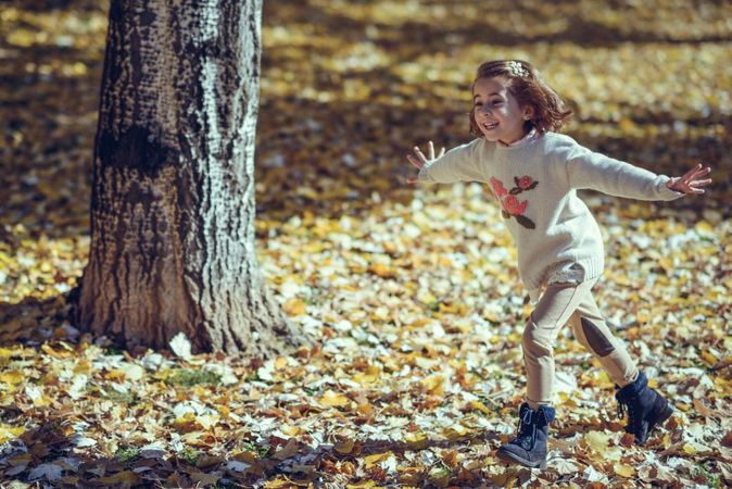 Joyful girl running in park of colorful fall leaves with her arms open