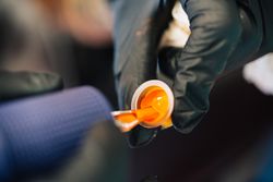 Hand holding a small pot of tattoo ink while loading up tattoo gun